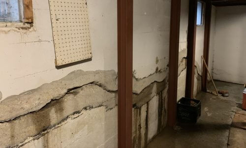 after photo of a severely bowed white poured basement wall straightened with the Gorilla Wall Braces basement bracing system installed along the basement wall