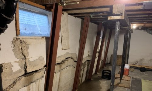 photo of a white poured concrete basement wall tipped in about 4 inches with Gorilla Wall Braces basement bracing system installed and ready to push the bowing basement wall back